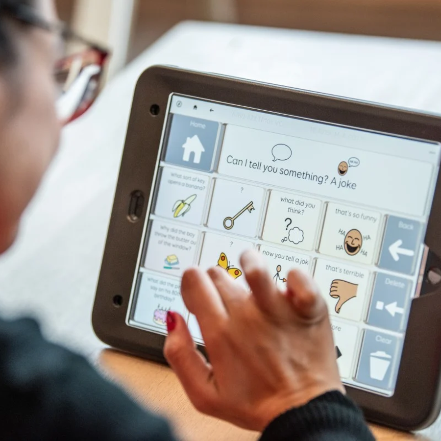 Person using a tablet with a symbol-based communication app, tapping icons on the screen.