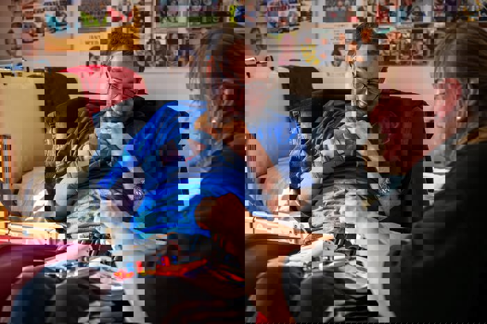 Carer supporting a man seated in a specialist chair, assisting him with an activity using adapted equipment at a tray table.