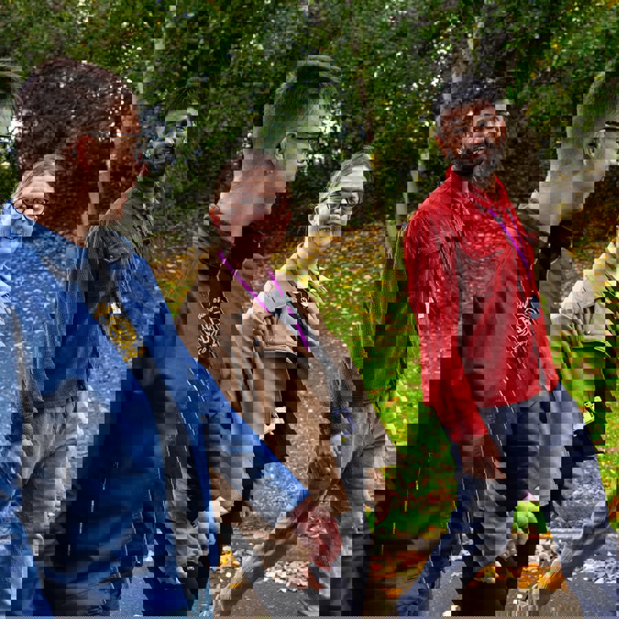 Three people walking together outdoors in a park, smiling and talking, with autumn leaves on the ground.