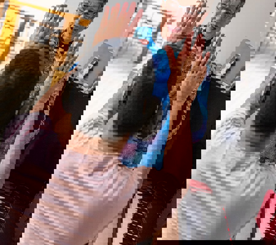 Older woman and young man wearing ear defenders share a high-five during a music session beside a piano.
