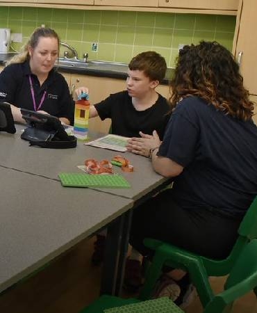 a boy and carers sat at a kitchen table.