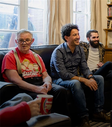three men sat on a settee in a front room talking and laughing.