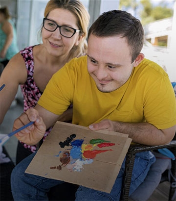 young man and his carer painting a picture.