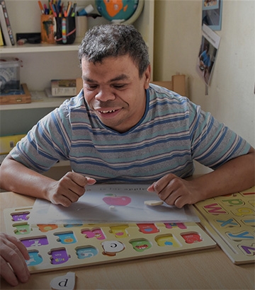man sat at table happily playing puzzles.