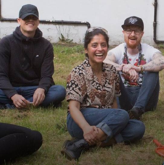 three young adults sat on grass laughing.