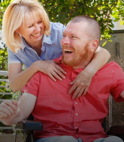 man in wheelchair smiling with his carer smiling and stood behind him.